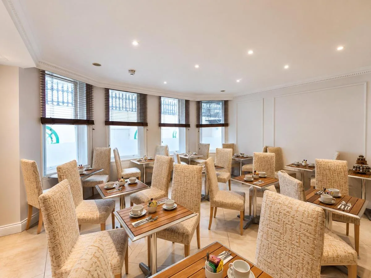 a dining room with tables and chairs and windows at Ashburn Hotel in London